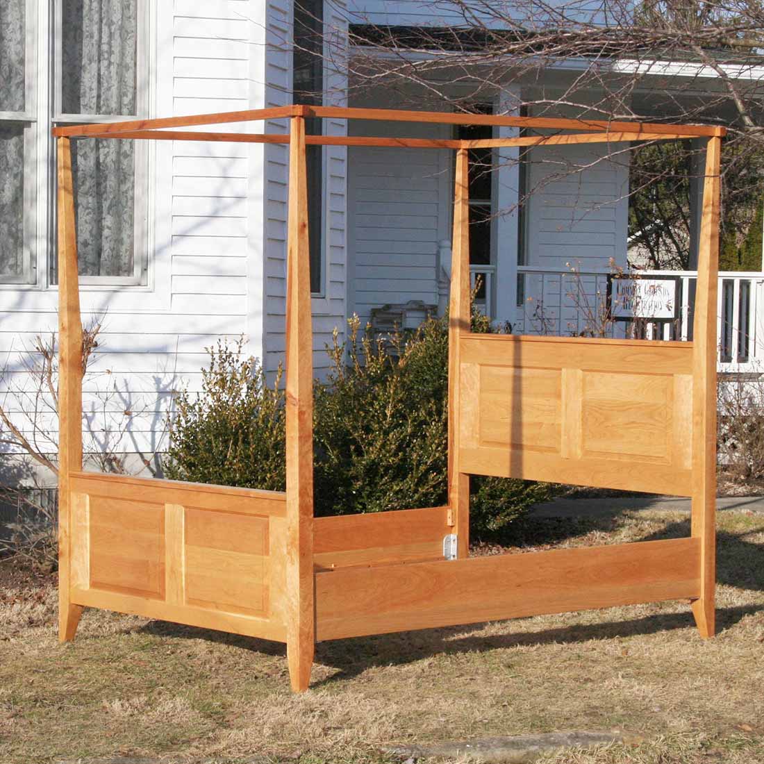side angled view natural wood canopy bed with paneled head and footboards