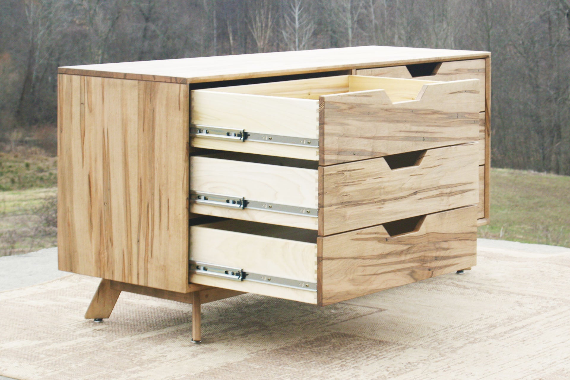 side angled view of Modern dresser with angled legs and three drawers open