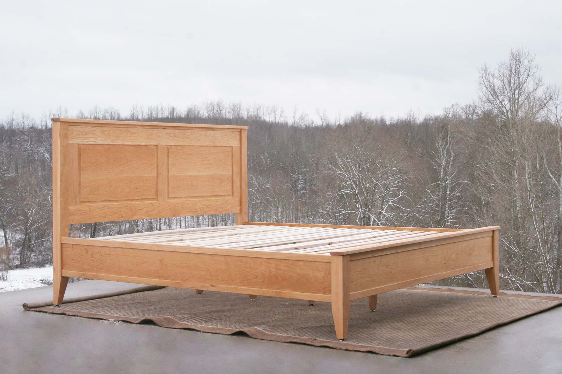 angled view side of hardwood Platform Bed with paneled headboard and tapered post