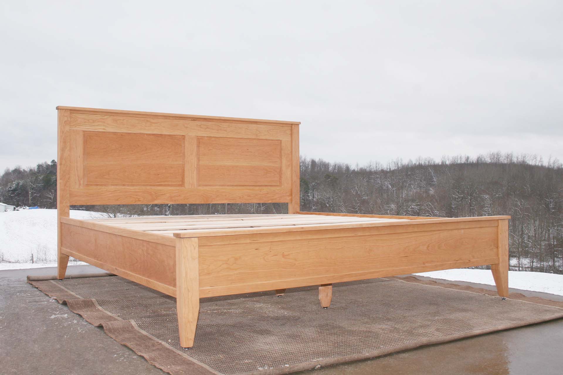 low angled view hardwood Platform Bed with paneled headboard and tapered post